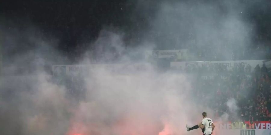 Dichte Rauchschwaden durchziehen das Mainzer Stadion, nachdem Feuerwerkskörper aus dem Gästeblock auf dem Rasen gelandet sind. Foto: Thomas Frey/dpa