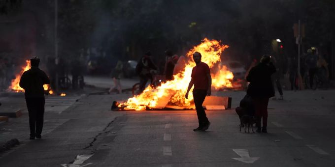 Demonstranten blockieren eine Strasse und stehen vor einer brennenden Barrikade. Proteste in Chile