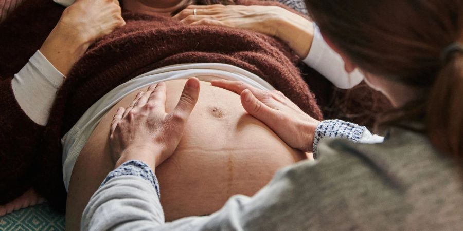 Eine Hebamme tastet in ihrer Berliner Praxis den Bauch einer schwangeren Frau ab.