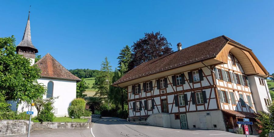 Wegweiser für die Fahrrad-Alpen-Panorama-Route-4 in Wattenwil. Hinten die reformierte Kirche und das alte Gemeindehaus.