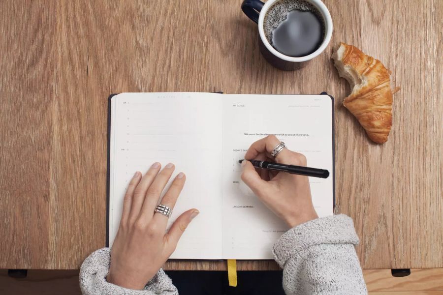 Notizbuch zwei Hände Croissant Kaffee notieren