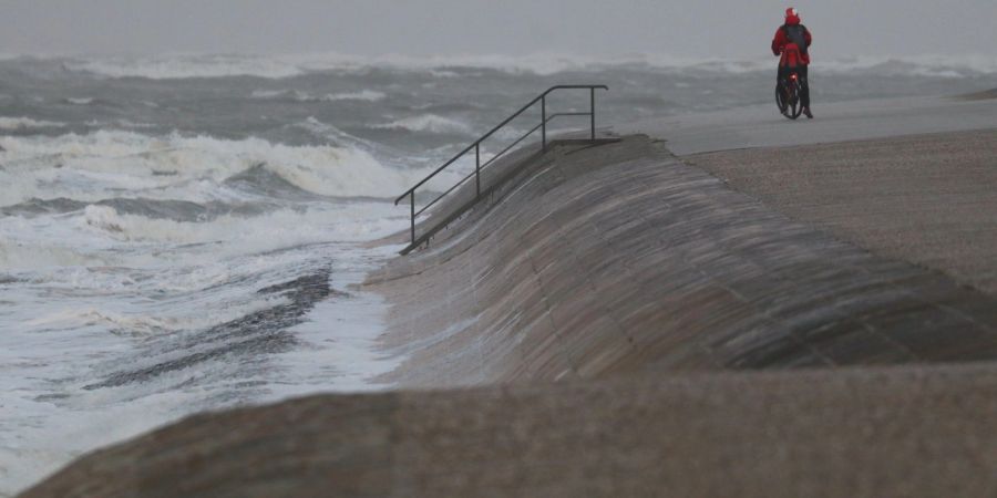 Eine Radfahrerin steht bei stürmischem Wetter an der Wasserkante auf der Insel Norderney. Ein Tiefausläufer sorgt für stürmisches Wetter im Norden.