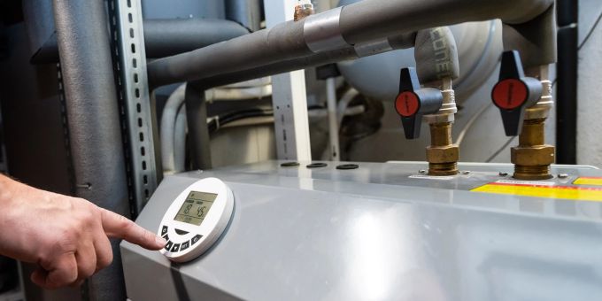 Ein Mann bedient eine Luftwärmepumpe, die im Keller eines Wohnhauses steht. Die Wärmepumpe gilt als die umweltfreundliche und zukunftssichere Alternative zur Öl- und Gasheizung. Hand Schalter Wärmepumpe Keller