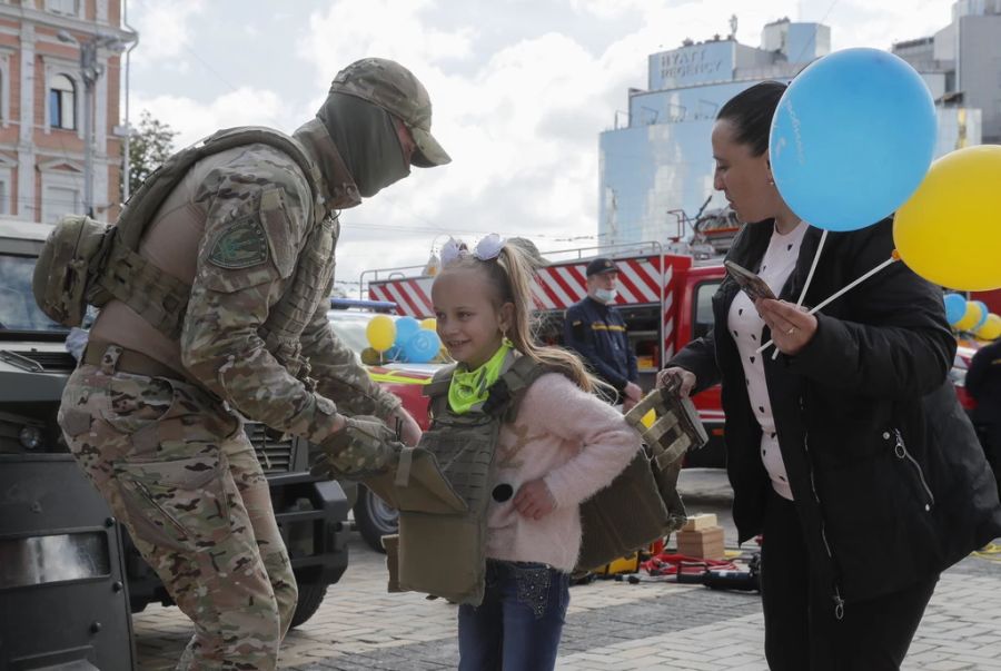 Ein ukrainischer Soldat zieht einem Mädchen eine kugelsichere Schutzweste über während einer gemeinsamen Ausstellung für Kinder der ukrainischen Polizei, Feuerwehr, Rettungskräfte und der Nationalgarde am 1. Juni 2021 in Kiew.