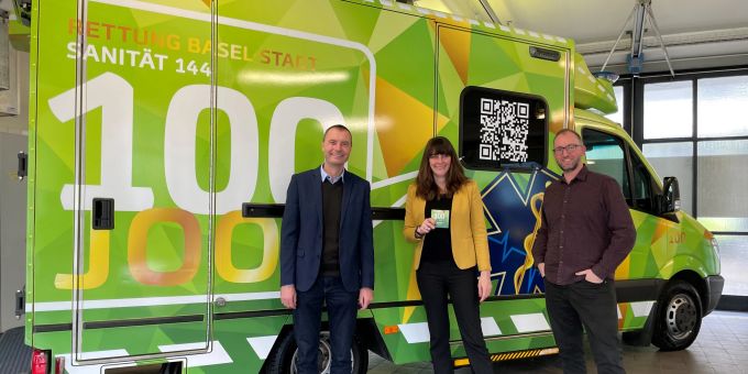 Martin Gabi, Leiter der Sanität Basel, Regierungsrätin Stephanie Eymann, Vorsteherin des Justiz- und Sicherheitsdepartements, und Daniel Kobler, Projektleiter «100 Joor Sanität Basel» vor dem Rettungswagen im Jubiläums-Look. Sanität