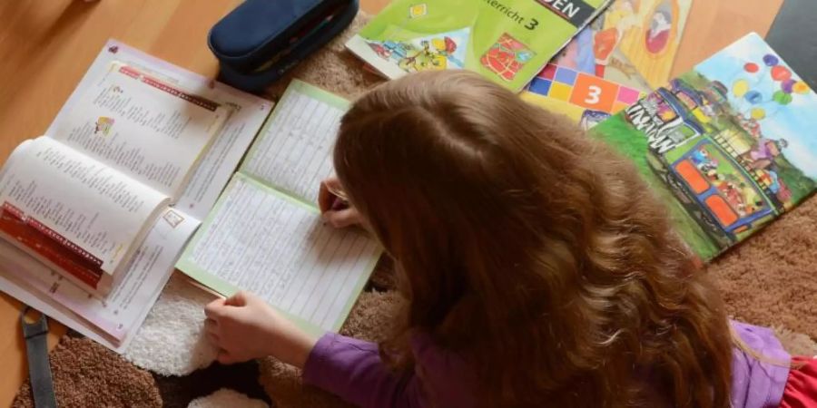 Ein Mädchen liegt auf einem Teppich in seinem Kinderzimmer und erledigt seine Hausaufgaben im Fach Deutsch. Foto: Jens Kalaene/dpa-Zentralbild/dpa