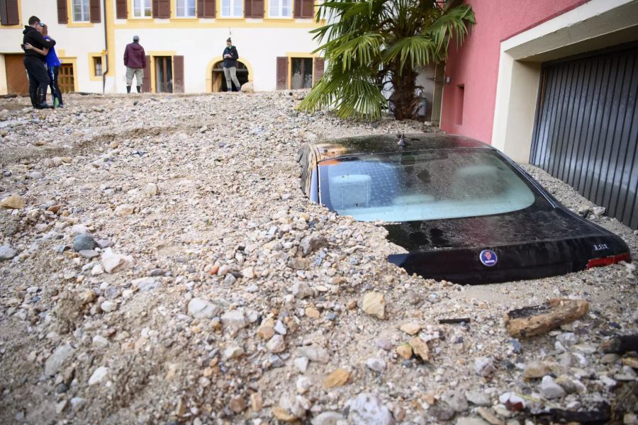 Dieser Saab wurde vom Geröll beinahe komplett zugeschüttet. Menschen im Hintergrund trösten sich nach dem heftigen Unwetter von letzter Nacht.