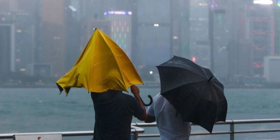 Menschen mit Regenschirmen kämpfen in Hongkong gegen starken Wind und Regen des Taifuns «Saola» an.