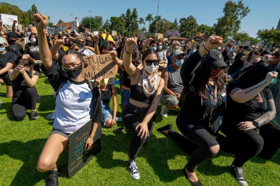 Demonstranten strecken ihre Fäuste in die Höhe und knien schweigend nieder im Village Green Park in Garden Grove.