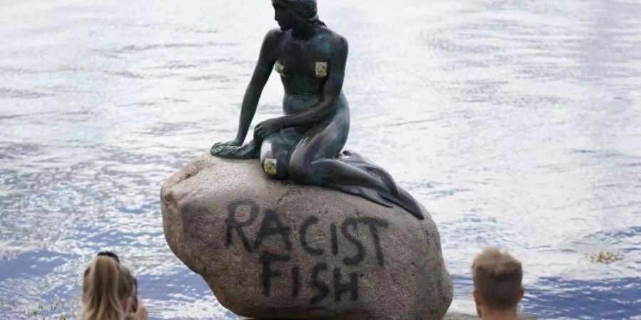 Polizeibeamte stehten an der Statue der kleinen Meerjungfrau, die von Unbekannten mit dem Schriftzug «Racist Fish» (Rassistischer Fisch) beschmiert wurde. Foto: Mads Claus Rasmussen/Ritzau Scanpix/AP/dpa