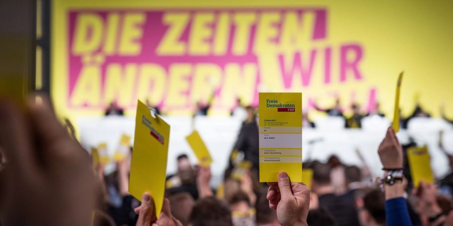 Delegierte halten beim ersten Präsenzparteitag der FDP nach dem Beginn von Corona die Stimmkarten hoch.