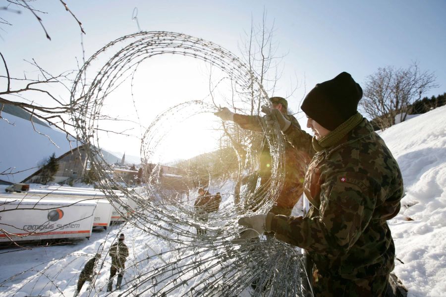 Aufbauarbeiten beim WEF 2009 in Davos, Verlegen von Stacheldrahtabschrankungen im verschneiten Gelände bei Sonnenuntergang.