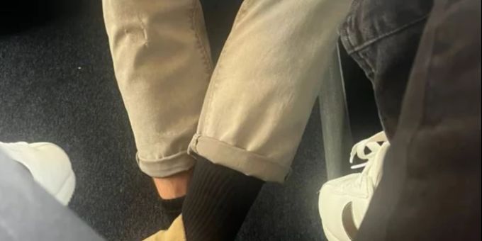 Manspreading im öffentlichen Verkehr. Der Mann streckt gemütlich seine Beine aus, die Frau nimmt ihre Füsse weg. Manspreading