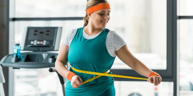 Plus-Size-Mädchen im Fitnessstudio beim Taillenmessen.