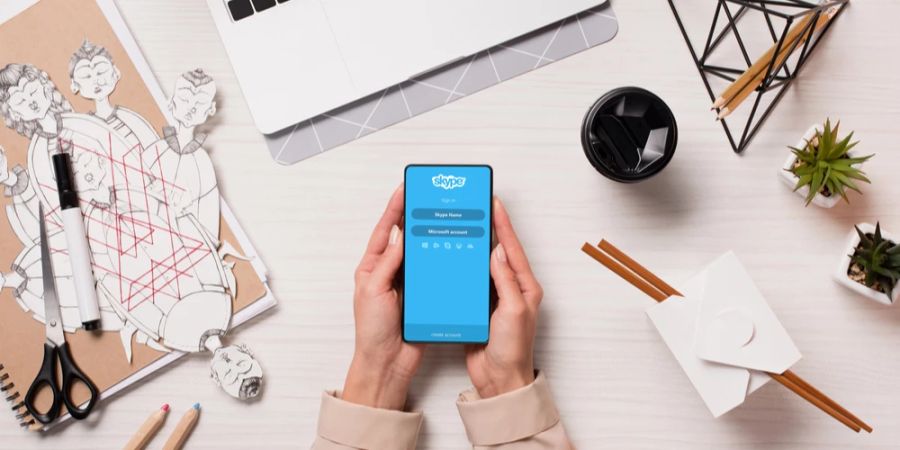 Skype auf Smartphone das in zwei Händen gehalten wird vor einem Schreibtisch