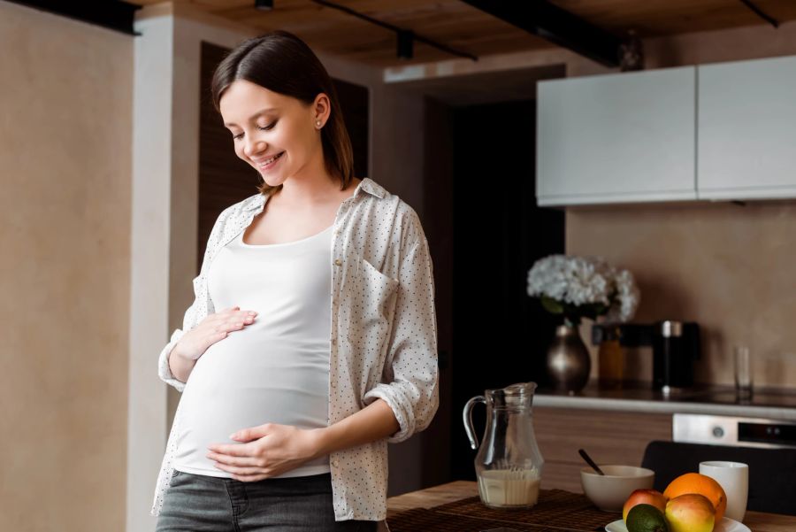 Glückliche Frau spricht zu ihrem ungeborenen Kind und hält ihren Bauch