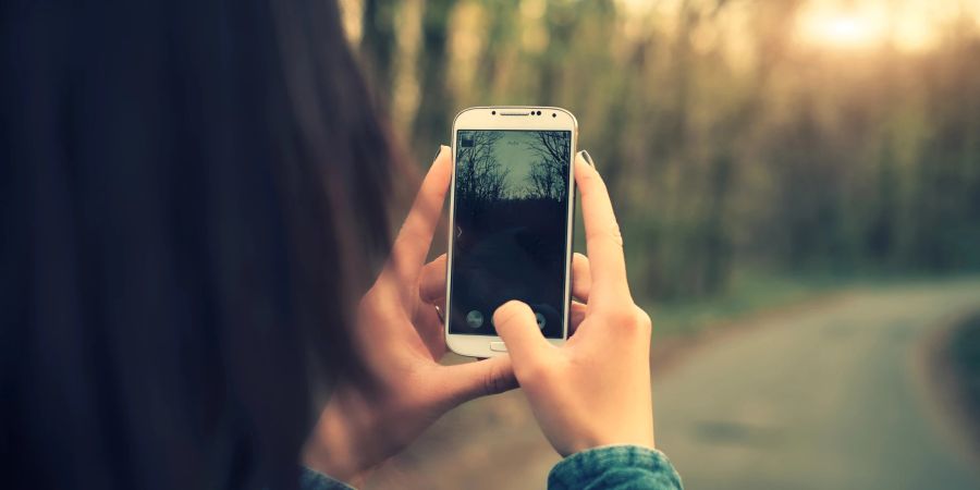 Frau fotografiert einen Wanderweg mit dem Smartphone