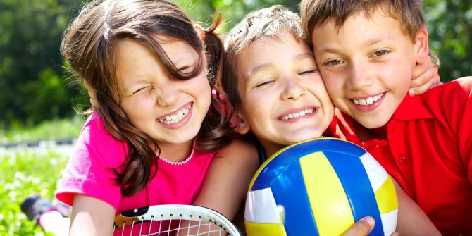 Glückliche Kinder mit Fussball und Tennisschläger.