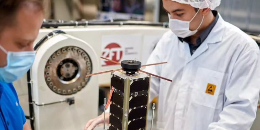 Zwei Mitarbeiter bereiten einen NetSat-Satelliten zum Test auf dem hochdynamischen Drehtisch vor. Foto: -/Zentrum für Telematik Würzburg/dpa