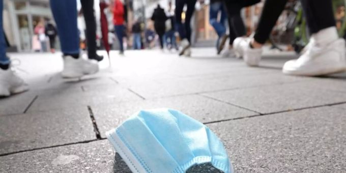 In einer Fussgängerzone gehen Menschen an einer auf dem Boden liegenden Mund-Nasen-Bedeckung vorbei. coronavirus vorbei