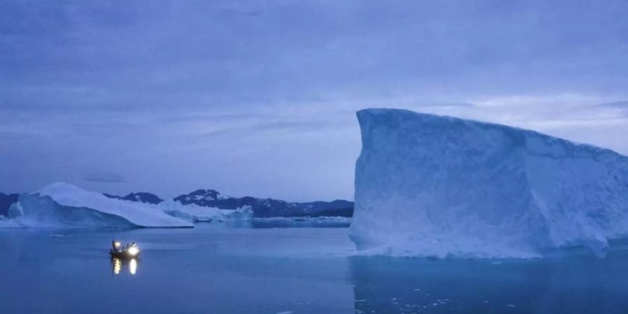 Ein Boot umfährt in der Dämmerung einen Eisberg auf Grönland. Foto: Felipe Dana/AP