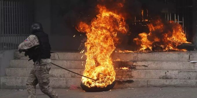 Ein Polizist entfernt einen brennenden Reifen vor einem Regierungsgebäude. Bei den Protesten gegen Haitis Regierung ist es in der Hauptstadt Port-au-Prince zu schweren Krawallen gekommen. Foto: Dieu Nalio Chery/AP Ein Polizist entfernt einen brennenden Reifen vor einem Regierungsgebäude. Bei den Protesten gegen Haitis Regierung ist es in der Hauptstadt Port-au-Prince zu schweren Krawallen gekommen. Foto: Dieu Nalio Chery/AP