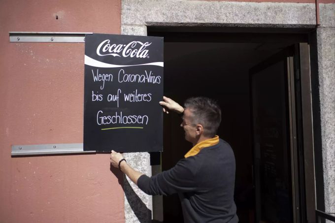 16.03.2020, Schweiz, Chur: Linus Caduff hängt ein Schild vor das Cafee Arcas mit der Aufschrift "Wegen Coronavirus bis auf weiteres geschlossen". Die Bündner Regierung hat beschlossen, wegen des Coronavirus weitere Massnahmen vorzunehmen. Einkaufsläden und Gastronomiebetriebe müssen ab heute 12:00 Uhr geschlossen sein. Foto: Gian Ehrenzeller/KEYSTONE/dpa +++ dpa-Bildfunk +++ Coronavirus · Schweiz