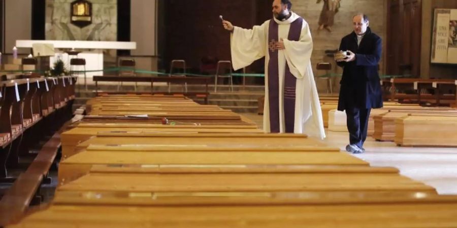 Ein Priester segnet Särge in Seriate, einer Gemeinde in der italienischen Provinz Bergamo. Foto: Antonio Calanni/AP/dpa