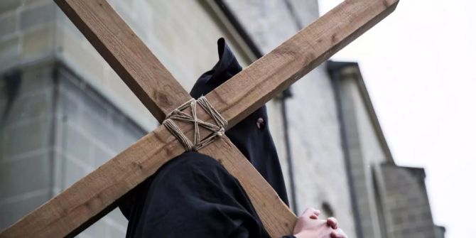 Ein Mann trägt zum Karfreitag ein Kreuz vor der Kirche in Romont FR.