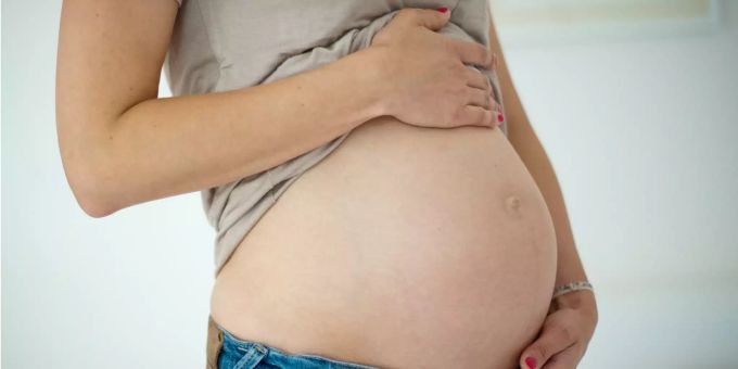 Eine junge Frau hält ihren Babybauch. Eine junge Frau hält ihren Babybauch.