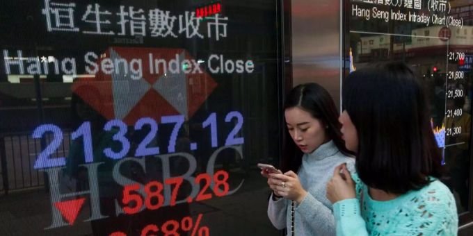 Zwei Frauen laufen an einem Schild vorbei, das Zahlen des Hang Seng Index zeigt. Hang-Seng-Index