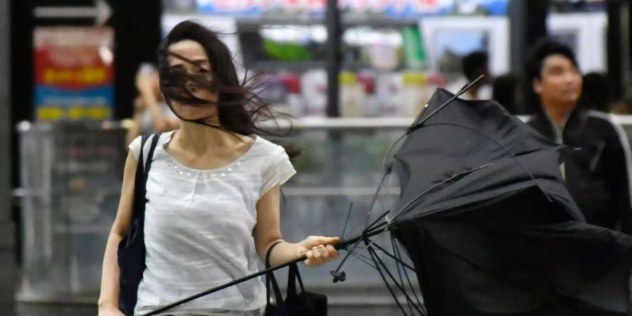 Eine Frau geht mit einem kaputten Regenschirm über eine Strasse nachdem Taifun «Jebi» die Region erreichte. (Symbolbild)