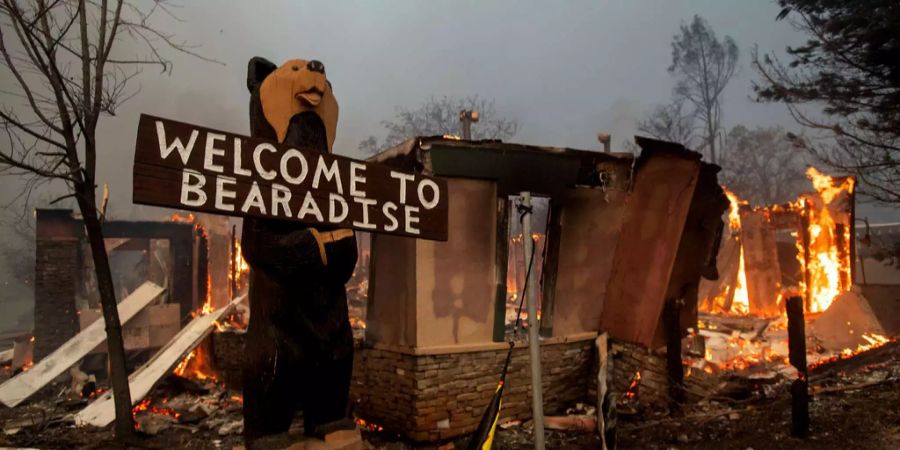 Ein Schild mit der Aufschrift «Welcome to Bearadise» steht vor einem vom Feuer zerstörten Gebäude.