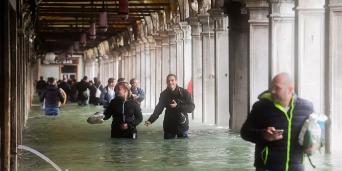 Touristen bahnen sich unter den Arkaden am überfluteten Markusplatz in Venedig ihren Weg. Schwere Unwetter haben fast ganz Italien getroffen und das öffentliche Leben teils lahmgelegt.