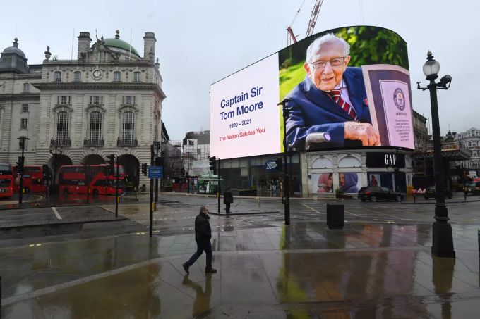 03.02.2021, Grossbritannien, London: Ein Bild des verstorbenen Kapitäns Sir Tom Moore ist als Tribut am Piccadilly Circus auf einer Anzeigentafel zu sehen. Captain Tom nach Corona-Infektion gestorben