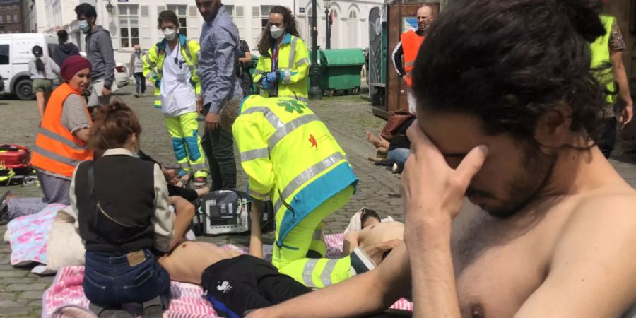 Ein Migrant fasst sich vor der Kirche «Saint-Jean-·Baptiste au Beguinage» an den Kopf, während Mitarbeiter des Gesundheitswesens mehrere Menschen behandeln (Archivbild) Foto: Nils Quintelier/BELGA/dpa