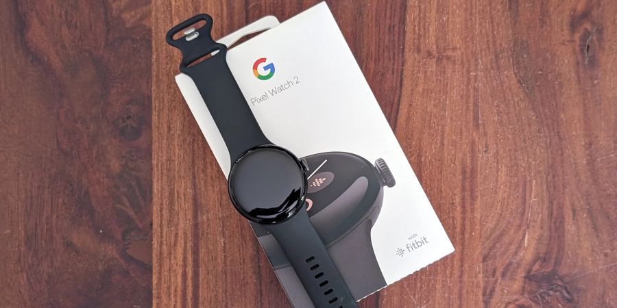 Auf einem Holztisch liegt eine Google Pixel Watch 2 auf ihrer Verpackung.