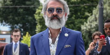 Mann mit grauem Bart und Sonnenbrille, blauer Blazer.