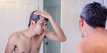 mann beäugt graue haare kritisch im spiegel