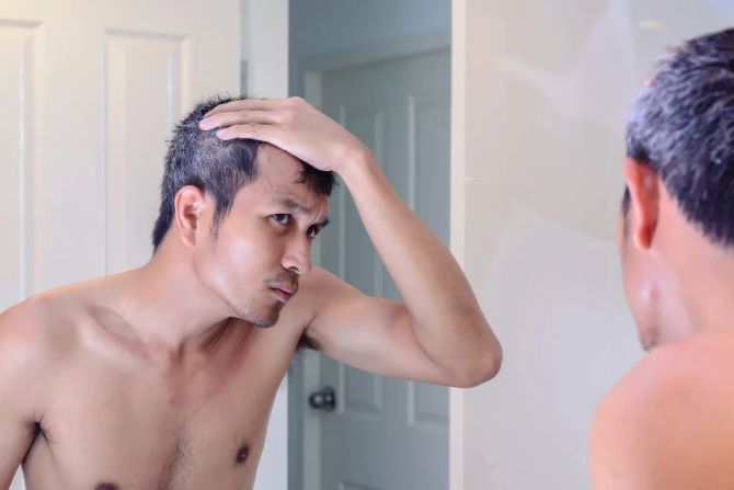 mann beäugt graue haare kritisch im spiegel