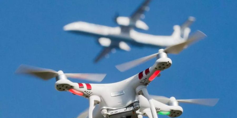 Eine private Drohne fliegt in knapp 10 Metern Flughöhe über einem Garten, in weiter Entfernung ist ein Flugzeug beim Anflug auf den Flughafen Düsseldorf zu sehen ist. Foto: Julian Stratenschulte/dpa