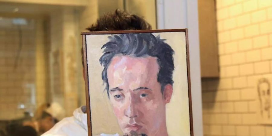 Sebastian Brecht hält sich ein Portrait vor sein Gesicht, das die Künstlerin Alix Bailey von ihm gemalt hat. Foto: Marie Weigl/dpa