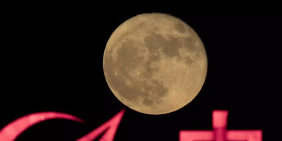 Der Supermond erhebt sich über einem Logo für ein chinesisches Staatsunternehmen. Foto: Ng Han Guan/AP/dpa