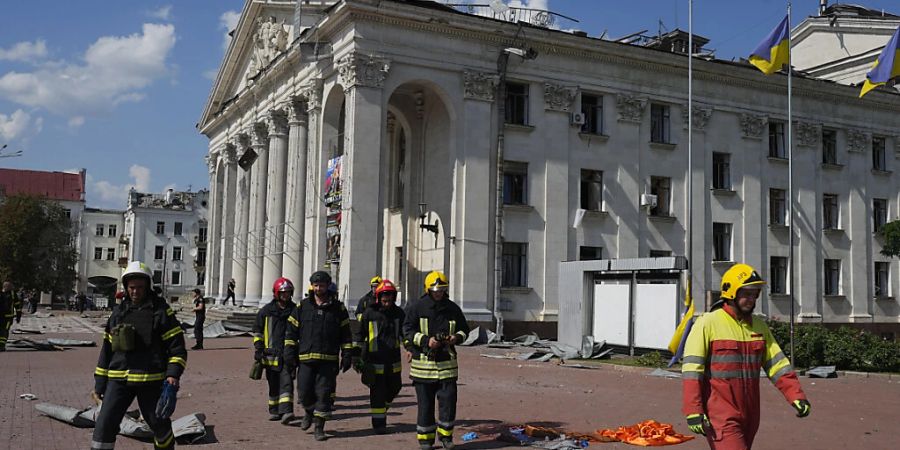 Feuerwehrleute gehen neben dem akademischen ukrainischen Musik- und Dramatheater Tschernihiw, das durch einen Angriff beschädigt wurde. Foto: Efrem Lukatsky/AP/dpa