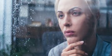 Eine junge Frau blickt mit neidischem Ausdruck durch das Fenster.