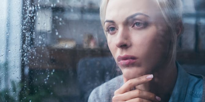 Eine junge Frau blickt mit neidischem Ausdruck durch das Fenster.