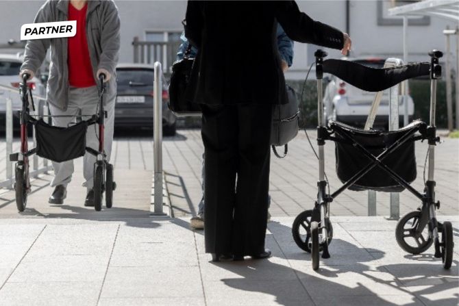 Zwei Personen sind mit einem Rollator unterwegs.