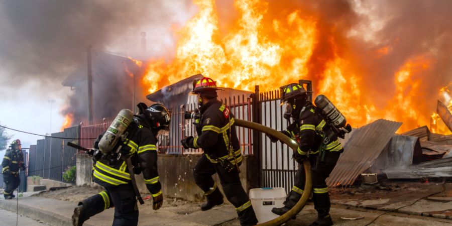Feuerwehrleute bekämpfen ein Feuer in einem Haus, während Waldbrände lodern. Foto: Javier Torres/AP/dpa