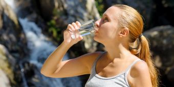 Junge Frau trinkt Wasser am Wasserfall.