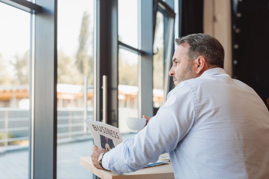 mann schaut aus dem fenster, business-zeitung in der hand